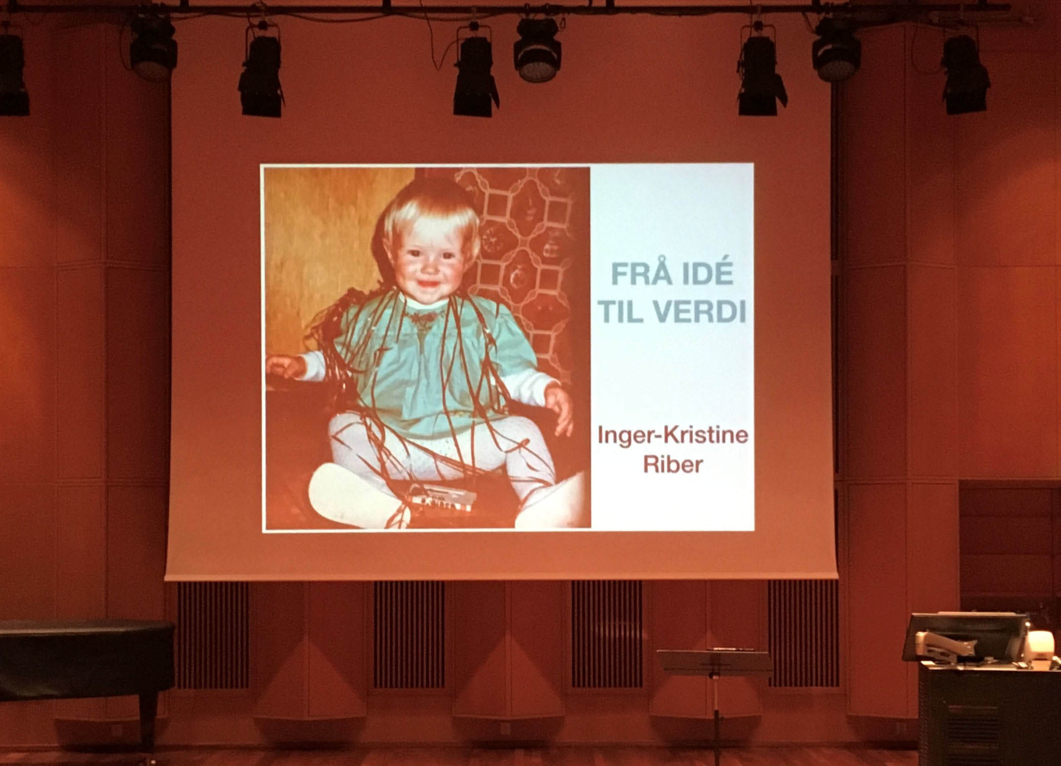 Presentasjonen til Inger Kristine vist på storskjerm i en sal. Bildet viser et barn og teksten "Frå idé til verdi".