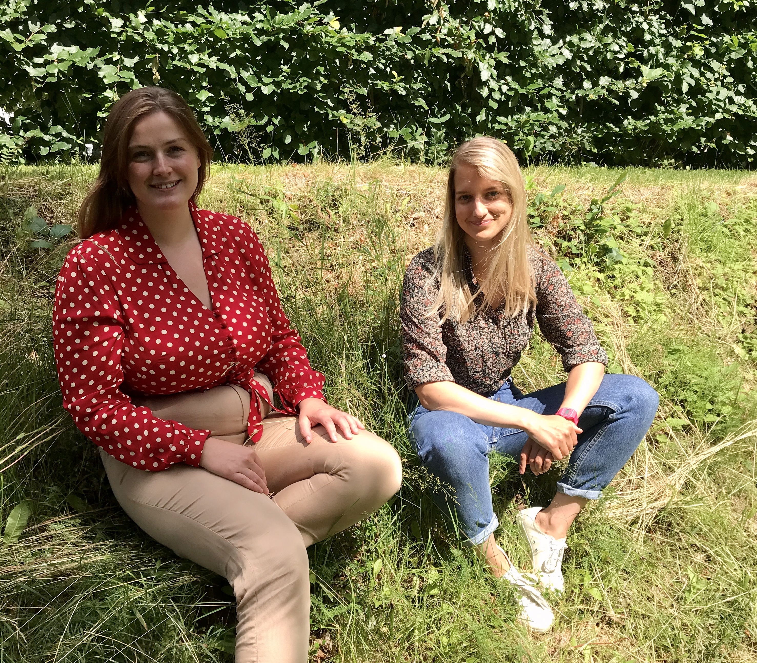 To jenter sitter ute i sola på en plen.
