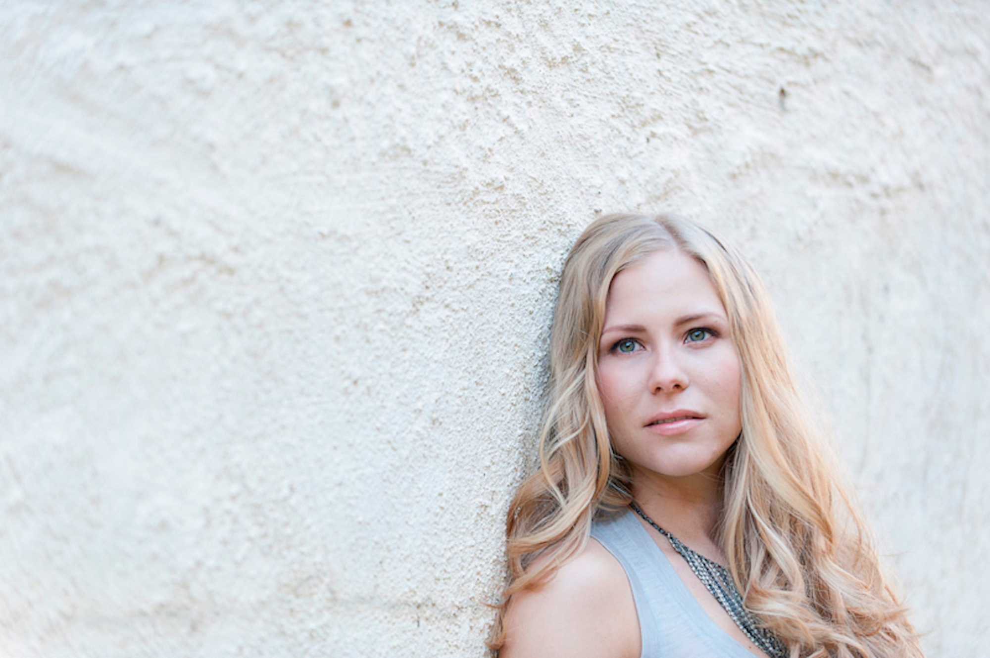 Ida står inntil en lys murvegg og ser mot venstre ut av bildet.