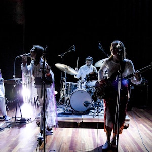 Fem studenter står og spiller på en scene – en på datamaskin, en på trommer, en på gitar, en på bass og en vokalist.