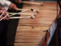 Nærbilde av marimba og 5 køller som spiller. Skimter så vidt hendene til tre personer som spiller samtidig