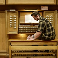 En student sitter foran orgelet i Lindemansalen og skriver noe på et ark.