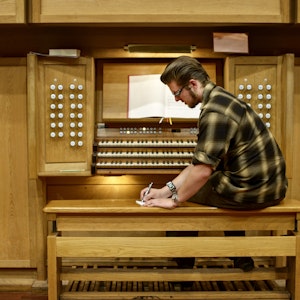 En student sitter ved et orgel og noterer på et ark som ligger ved siden av ham på krakken.