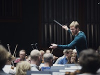 En dirigent veiver oppglødd dirigentstaven sin foran et orkester.