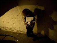 En mann går ned en spiraltrapp omringet av hvit mur, bærende på en saksofon og et noteark.