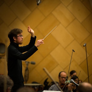 Nils Erik Måseidvåg står foran Kringkastingsorkesteret med begge hendene i været. Den ene hånda holder kan dirigeringspinnen.