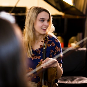 Student står smilende i et flygelrom og holder rundt en fiolin.