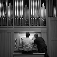 En student spiller på orgelet i Levinsalen. Læreren står ved siden av og peker på notearket.
