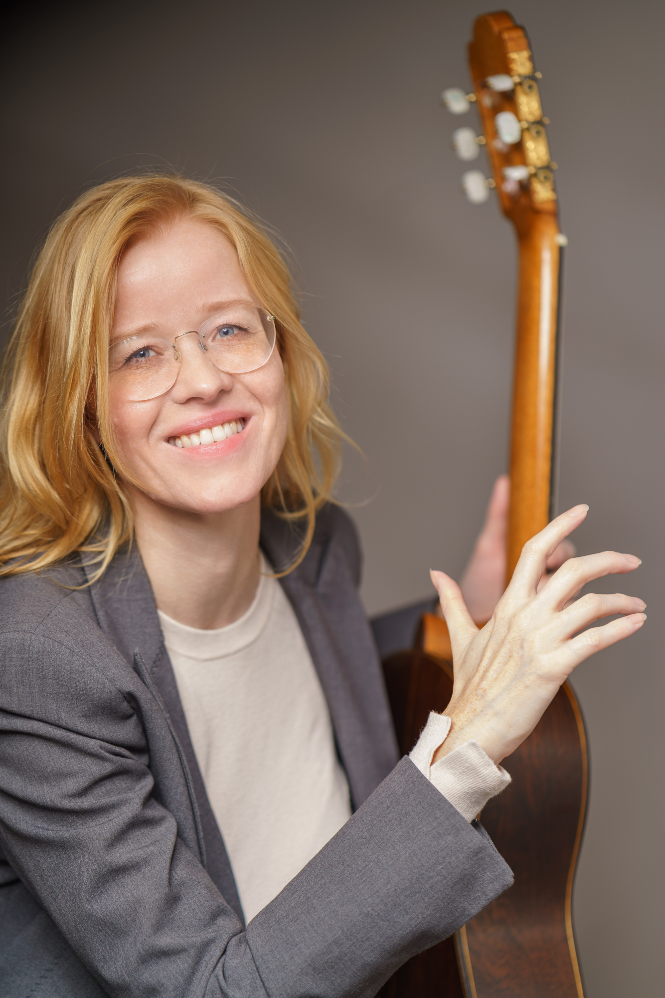 Eva står foran en vegg og holder opp en gitar. Hun smiler.