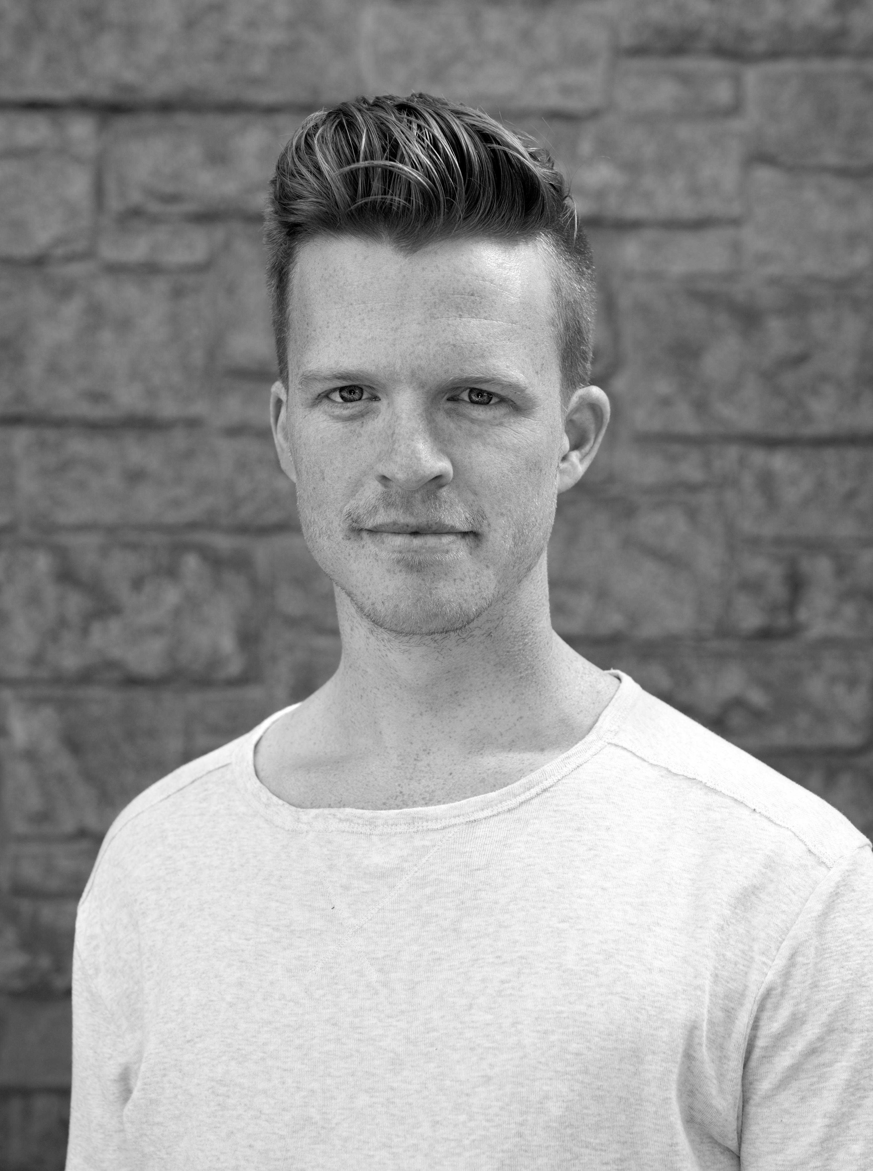 Jonas står foran en murvegg å ser rett inn i kameraet.