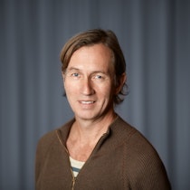 Morten is standing in front of a dark wall and smiling towards the camera.