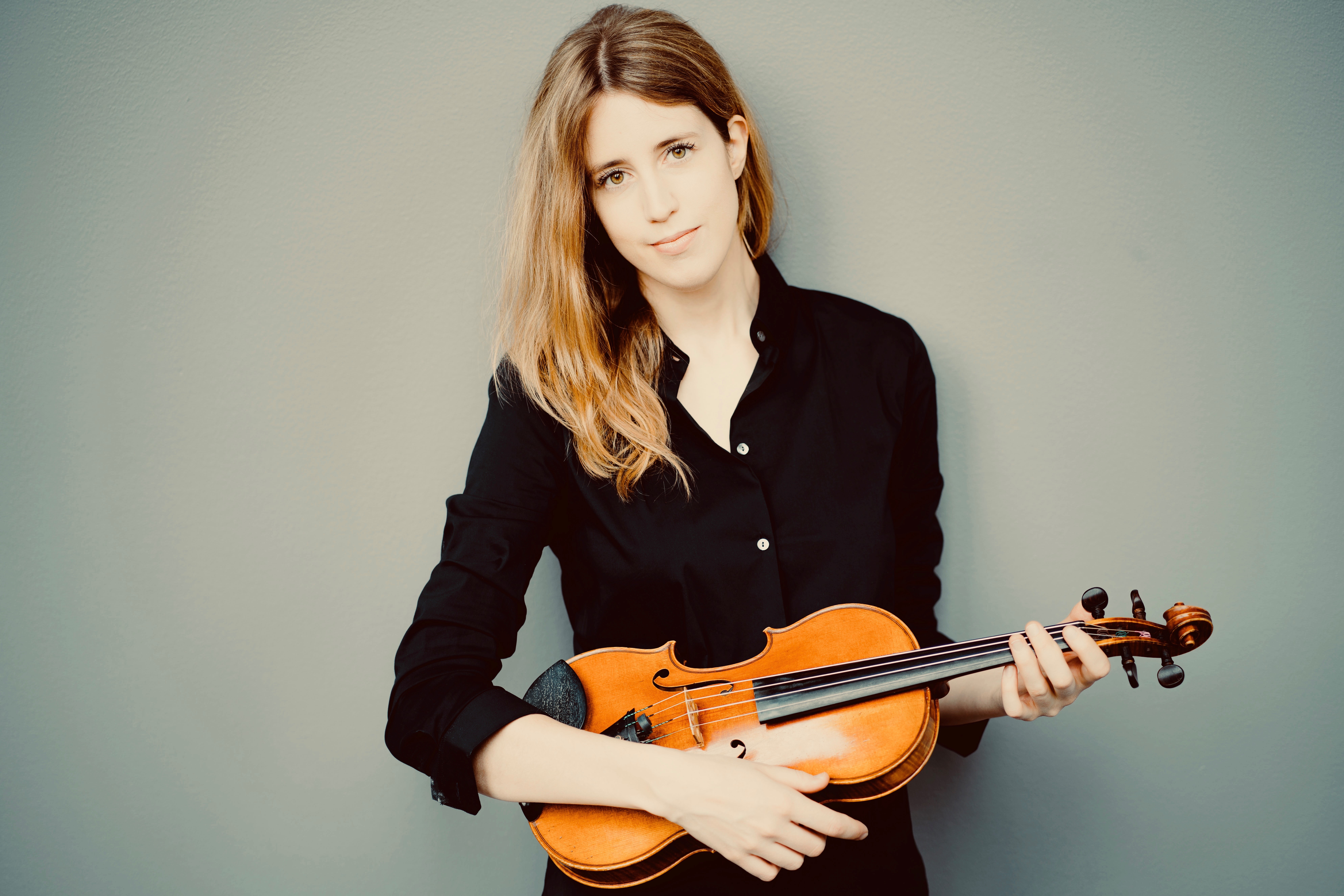 Vilde Frang står foran lys vegg med fiolinen i hendene.